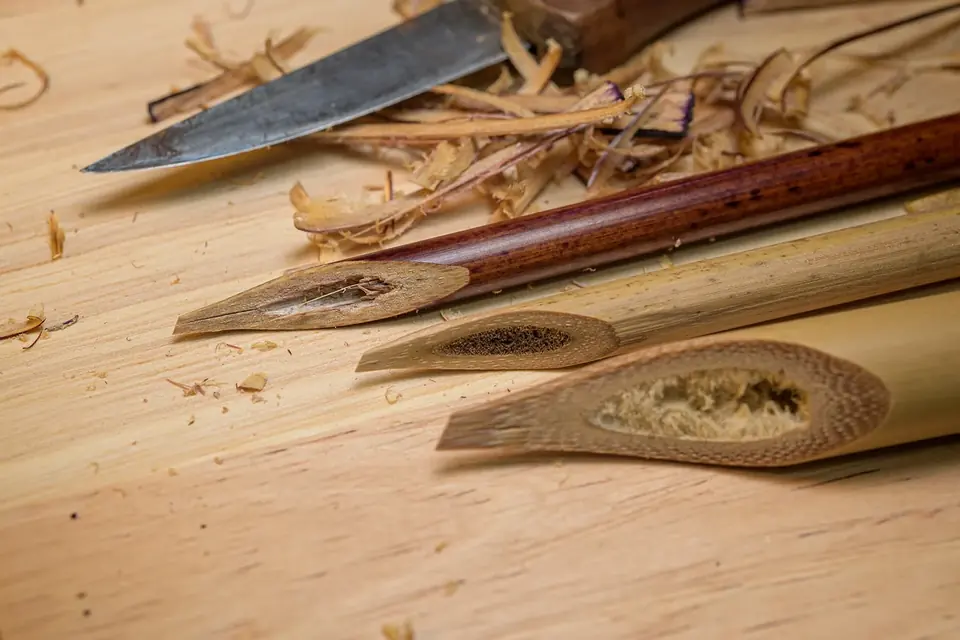 Plusieurs calames de roseau et de bambou taillés, posés à côté d'un couteau sur une table en bois