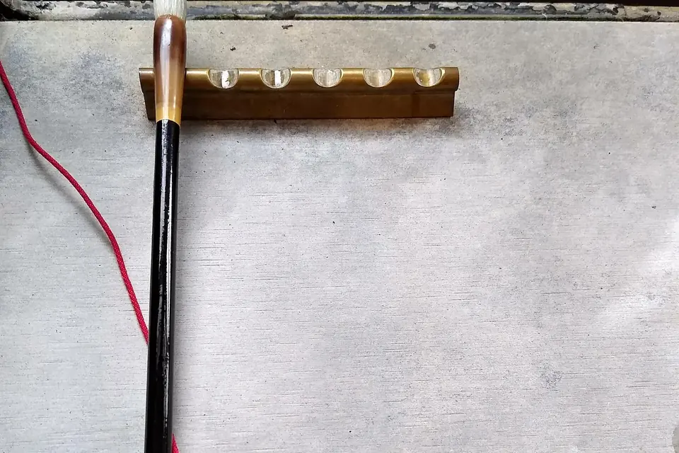 Pinceau de calligraphie à long manche sombre suspendu à un porte-pinceaux en bois, au-dessus d'une surface claire