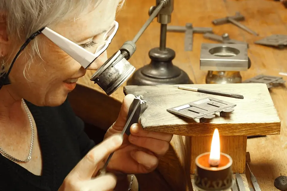 Une graveuse, loupe fixée à ses lunettes, travaille un petit poinçon d'acier au-dessus d'un établi