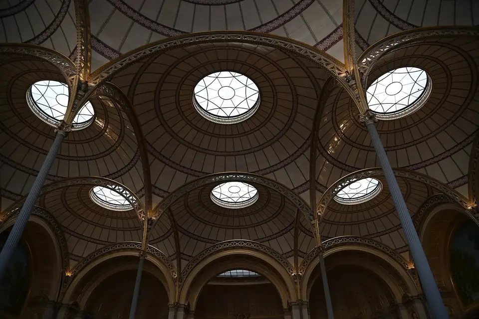Grande salle de lecture sous des coupoles de faïence blanche percées d'oculus, portées par de fines colonnes de fonte, avec des rangées de tables